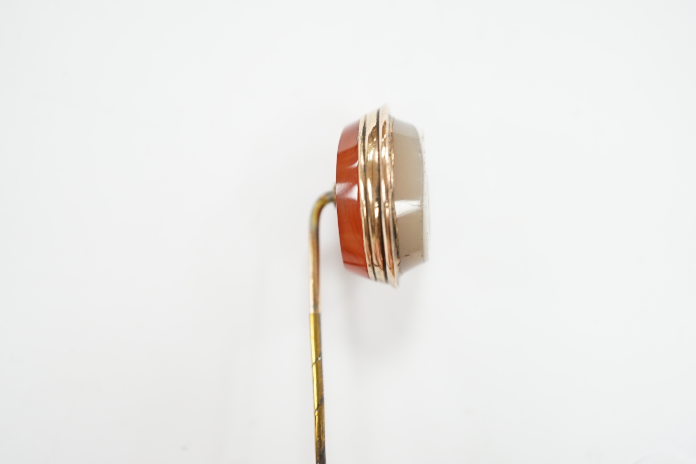 An early 20th century yellow metal and oval intaglio chalcedony set stick pin, 77mm.